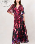 A woman modeling a long floral maxi dress with sheer flutter sleeves and a V-neckline, shown against a plain light background. The dress has a dark base with prominent magenta, pink, and purple floral patterns. Hope & Ivy