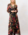 A woman modeling a long-sleeve maxi dress with a dark floral print, featuring a V-neckline and a tie at the waist, paired with dark brown boots against a plain studio background. Hope & Ivy