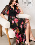 A woman models a black midi dress with a vibrant pink, red, and orange floral print while sitting in a white boucle armchair. The brand logo 'Petite' is visible in the top right corner.